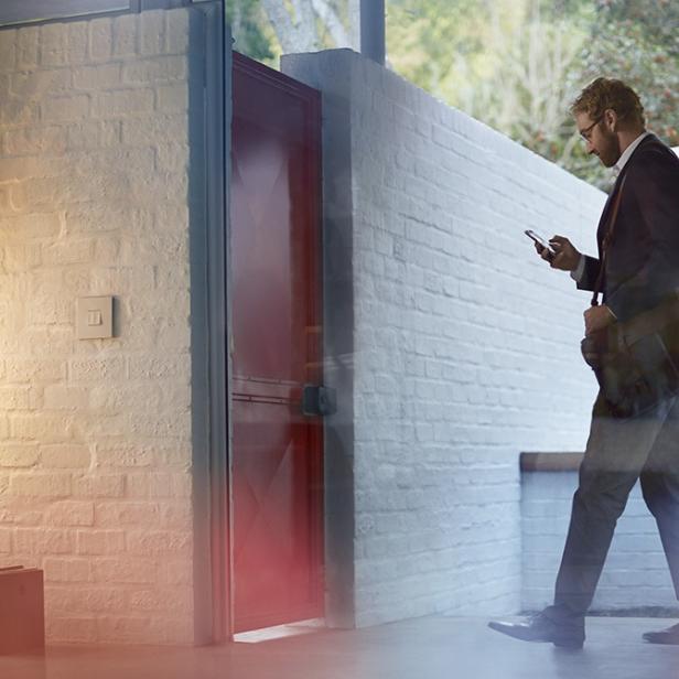 Ein Mann im Anzug geht in einem modernen Haus und schaut auf sein Smartphone.