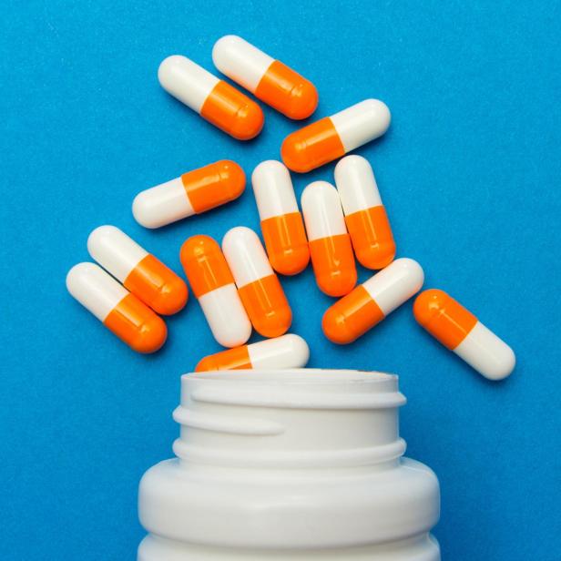 Orange white capsules (pills) were poured from a white bottle on a blue background. Medical background, template.