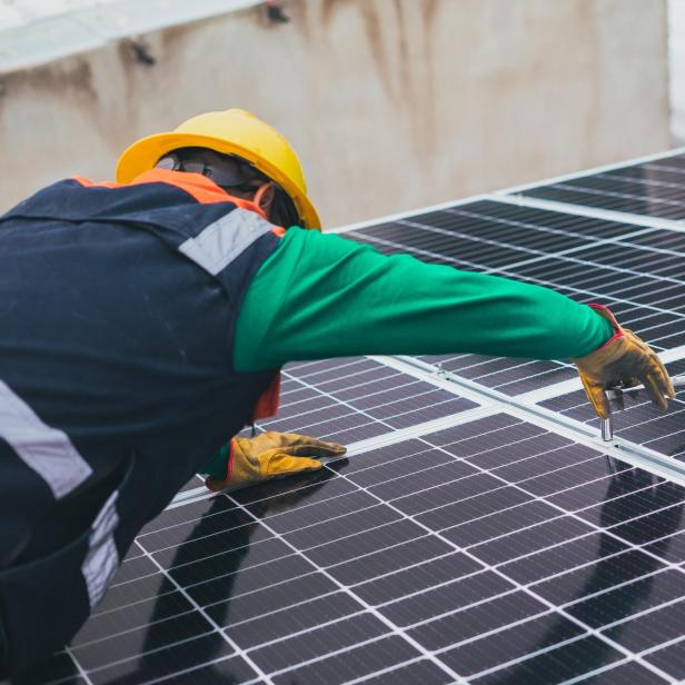 Ein Arbeiter mit Schutzhelm montiert Solarmodule auf einem Dach.
