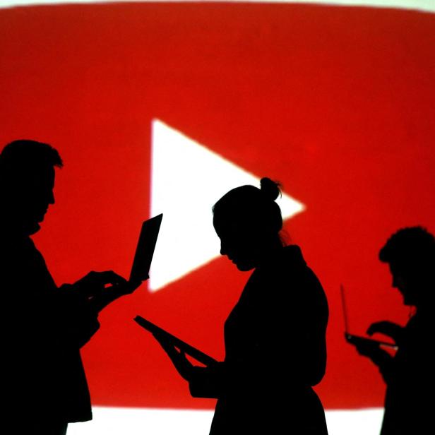 FILE PHOTO: Silhouettes of laptop and mobile device users next to a screen projection of the YouTube logo in this picture illustration