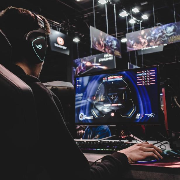 Ein junger Mann spielt ein Computerspiel mit Headset und blickt auf den Monitor.