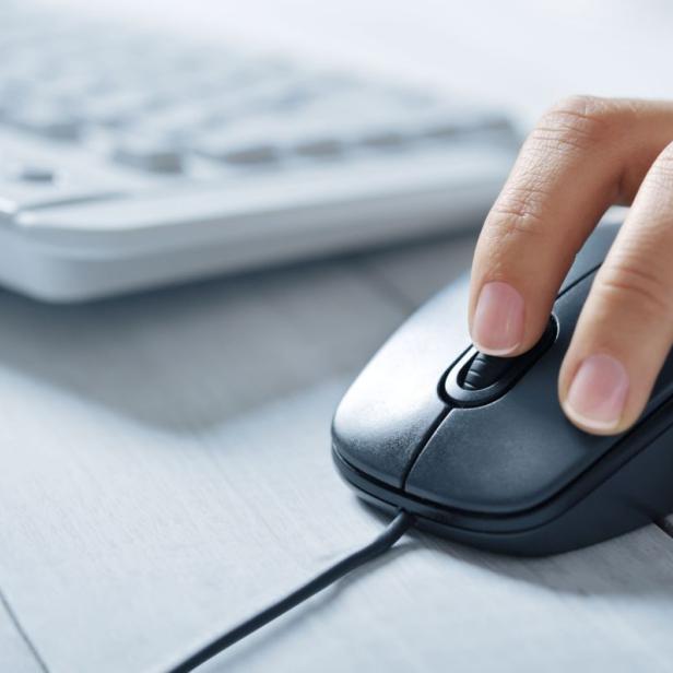 Eine Hand bedient eine Computermaus vor einer Tastatur.