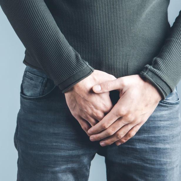 Man holding his urethra in pain on gray background