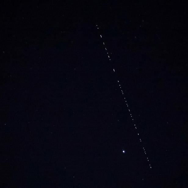 A train of Starlink communications satellites forms a single file of lights crossing the night sky, at Cape Matxitxako