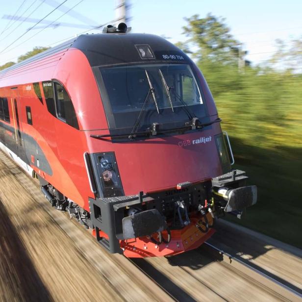 Ein roter ÖBB Railjet-Hochgeschwindigkeitszug fährt auf einer Bahnstrecke.