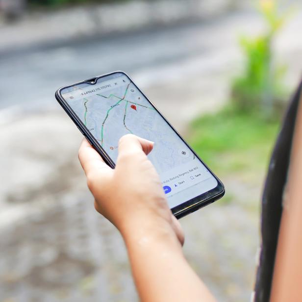 Eine Frauenhand hält ein Handy in der Hand mit Google Maps App.