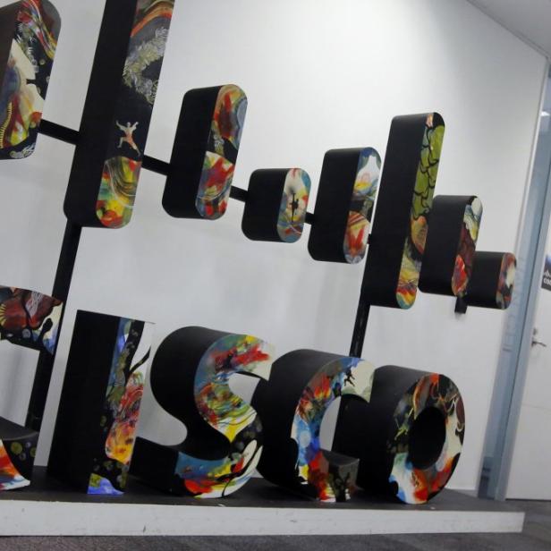 Eine Frau steht in einem Flur neben einer großen, bunten „Cisco“-Skulptur.