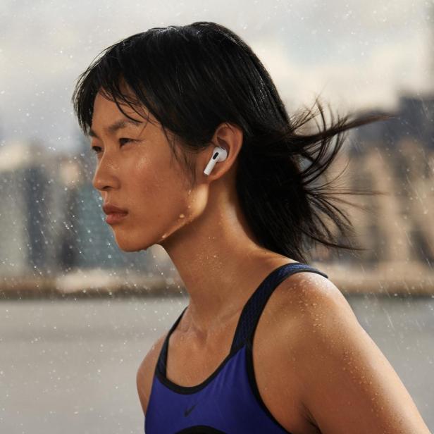 Läuferin trägt Apple AirPods im Regen vor einer Großstadt-Skyline