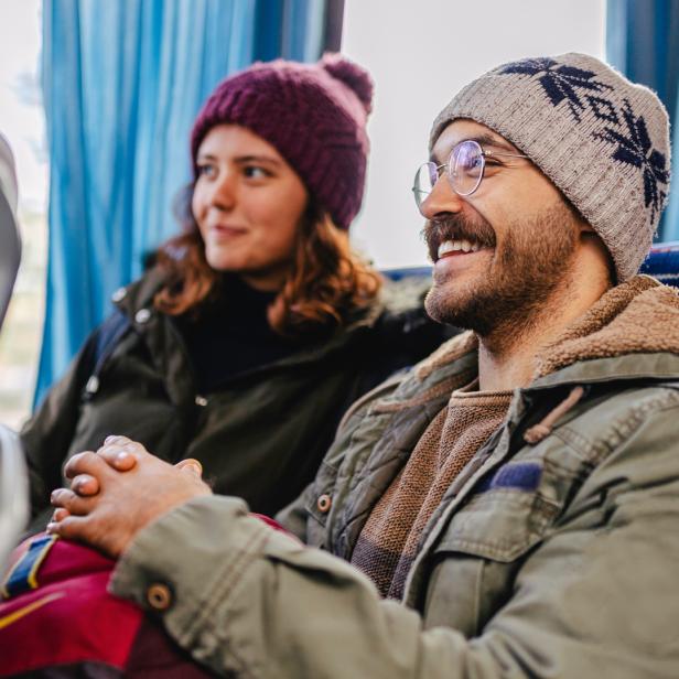 Zwei winterlich bekleidete Fahrgäste fahren gut gelaunt in einem Bus