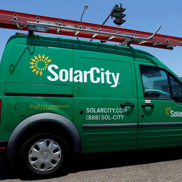 Ein grüner SolarCity-Lieferwagen mit einer Leiter auf dem Dach steht auf einer Straße.
