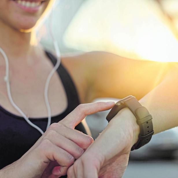 Close-up of athletic woman using fitness tracker at sunset.