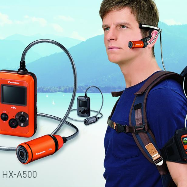 Ein Mann trägt eine Panasonic HX-A500 4K-Actionkamera mit Zubehör vor einer Bergkulisse.