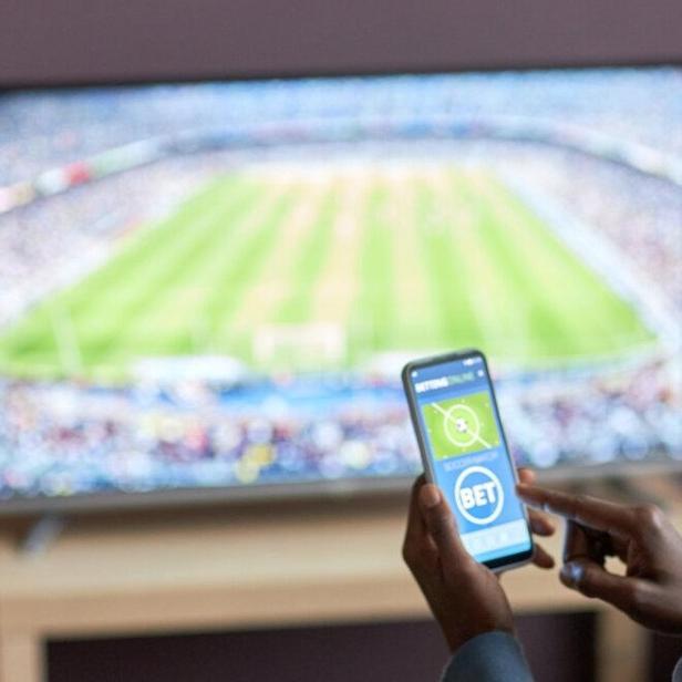 Ein Mann hält ein Smartphone mit einer Sportwetten-App auf dem Bildschirm