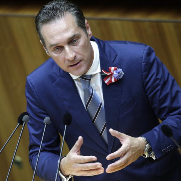 Ein Mann in einem blauen Anzug spricht an einem Rednerpult mit mehreren Mikrofonen.