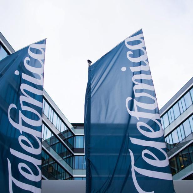 Zwei Flaggen mit dem Telefónica-Logo vor einem modernen Bürogebäude.