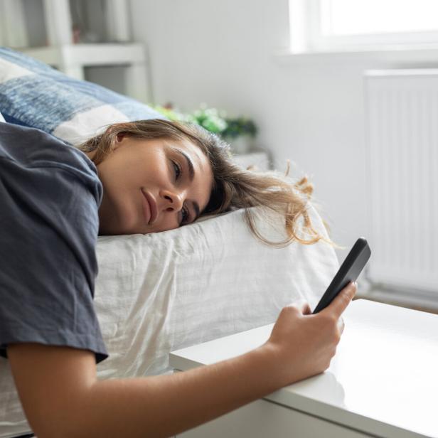 Eine Frau liegt im Bett und hält ein Smartphone in der Hand.