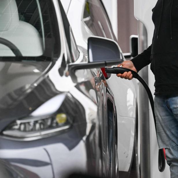 Mann lädt Tesla an Supercharger (Symbolbild)