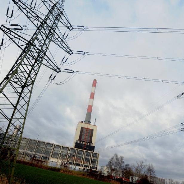Hochspannungsmasten und ein Schornstein vor einem bewölkten Himmel.