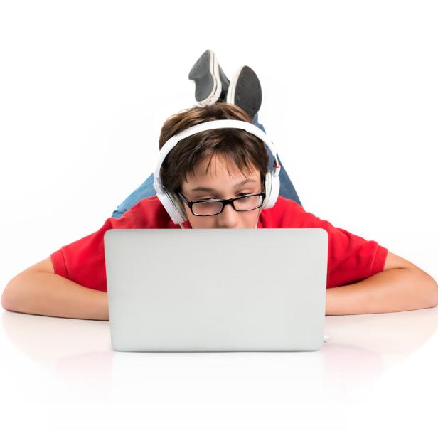 Ein Junge mit Brille und Kopfhörern liegt auf dem Boden und benutzt einen Laptop.