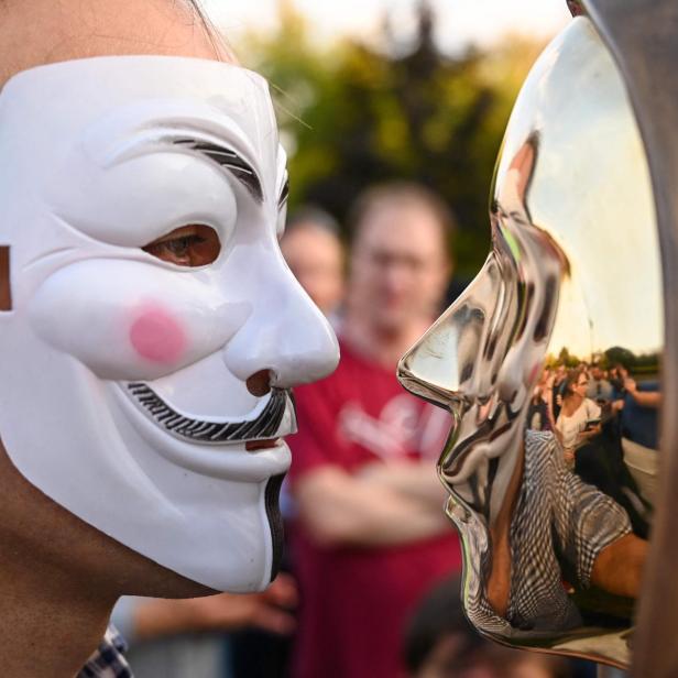 Mann mit Maske vor einer Statue von Satoshi Nakamoto in Budapest