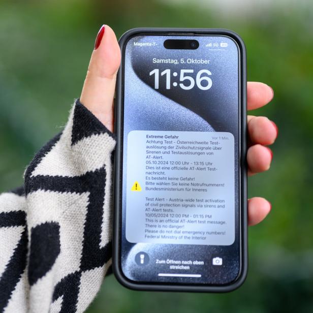Eine Hand hält ein Smartphone mit einer Warnmeldung des österreichischen Zivilschutzes.