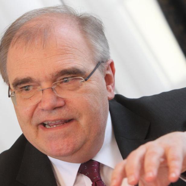 Ein Mann mit Brille, Anzug und Krawatte gestikuliert mit der Hand.