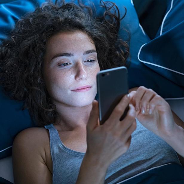 Eine Frau liegt auf einem blauen Kissen und schaut entspannt auf ihr Smartphone.