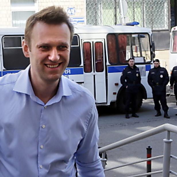 Alexei Nawalny lächelt vor einem Gefangenentransporter und Polizisten.