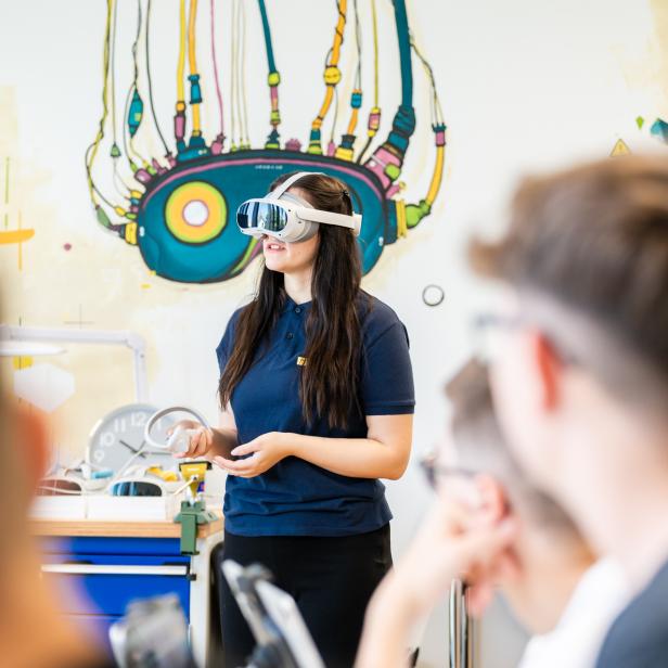 Eine Frau trägt eine Virtual-Reality-Brille in einem Klassenzimmer und erkundet digitale Lerninhalte.