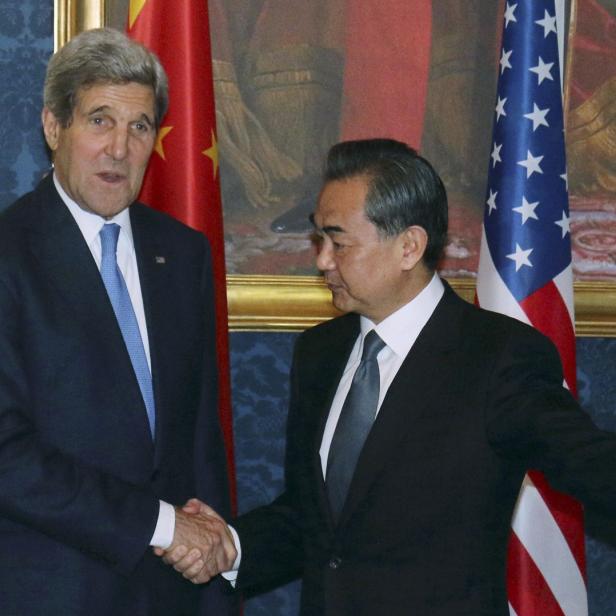 John Kerry schüttelt Wang Yi vor chinesischen und amerikanischen Flaggen die Hand.