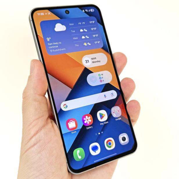 Eine Hand hält ein Smartphone, auf dessen Bildschirm Wetter- und Kalender-Widgets zu sehen sind.