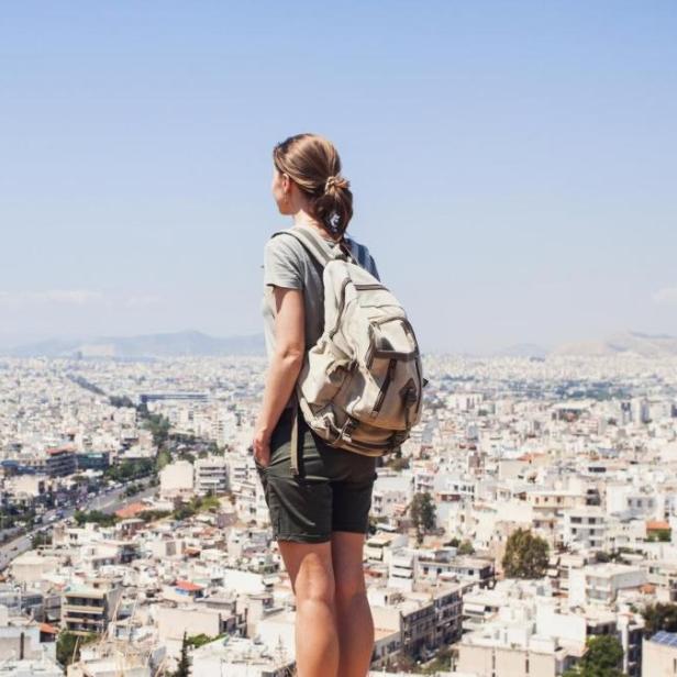 Eine Frau steht mit Rucksack auf einem Hügel über Athen
