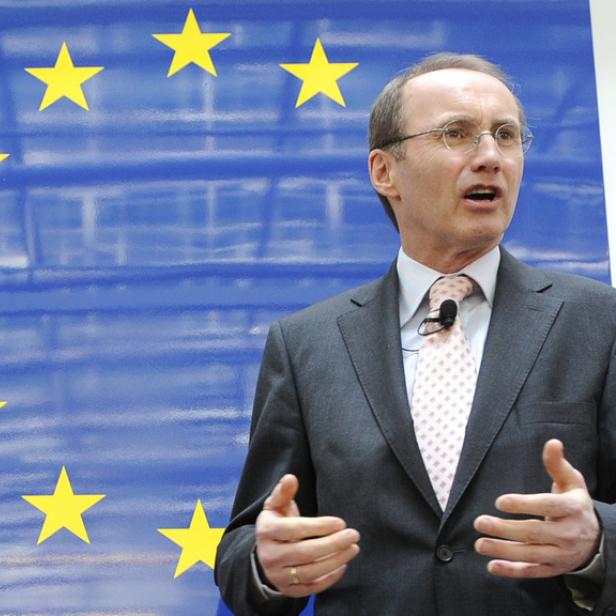 Ein Mann in Anzug gestikuliert vor einer EU-Flagge.