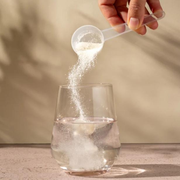 Eine Person kippt einen Löffel mit Basenpulver in ein Glas Wasser zum Auflösen.