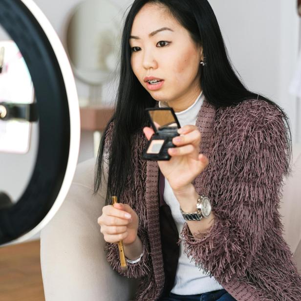 eine junge Frau hält eine Make-Up-Schatulle in eine Kamera mit Ringlicht