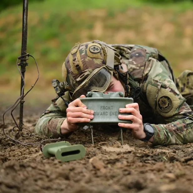 Ein Soldat stellt eine Claymore-Mine am Boden auf.