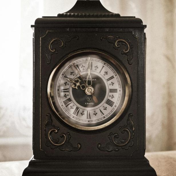 Eine alte, dekorative Tischuhr mit römischen Ziffern steht auf einem Tisch.