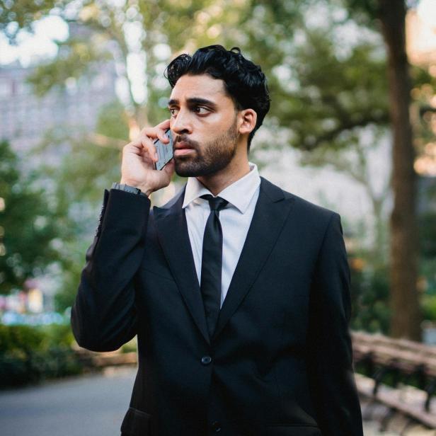 Anzugträger mit Smartphone am Ohr schaut skeptisch.