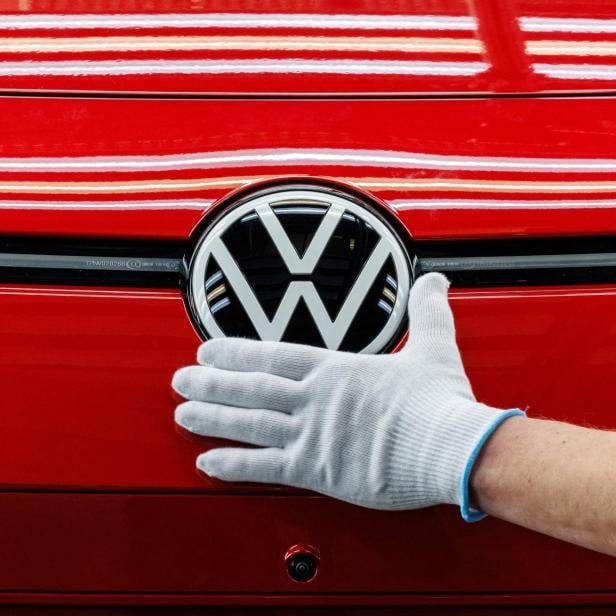 Nahaufnahme auf das VW Logo eines roten Fahrzeugs, daneben eine behandschuhte Hand