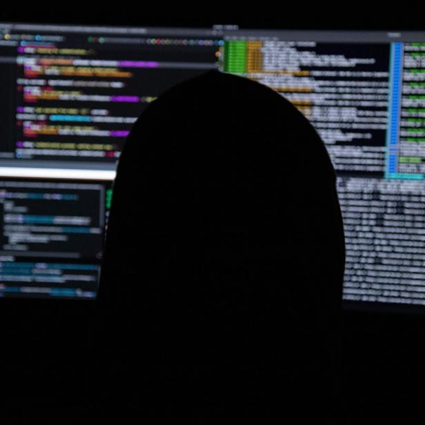 Symbolbild Scam: Man sieht eine Person von hinten, die vor mehreren Bildschirmen sitzt.