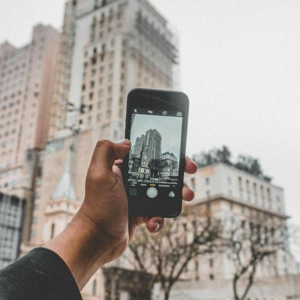 Eine Person fotografiert ein Gebäude mit einem Smartphone.