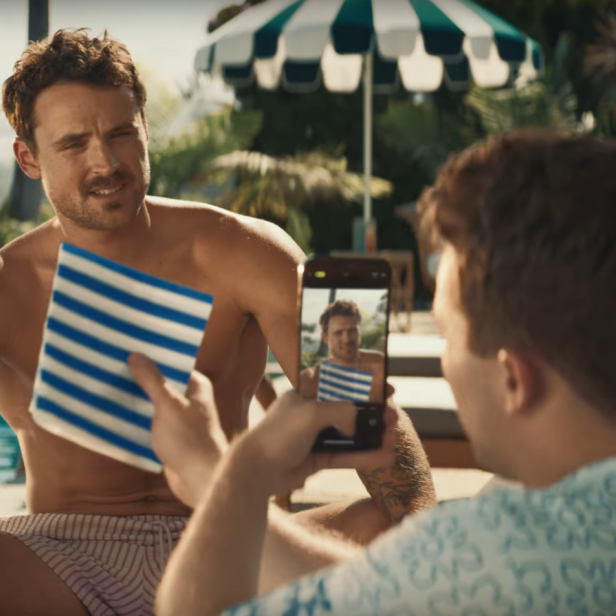 Ein Mann wird am Pool von einem anderen mit dem Handy fotografiert.