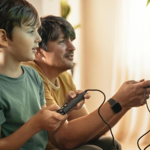 Vater und Sohn spielen auf einer alten Videospielkonsole.