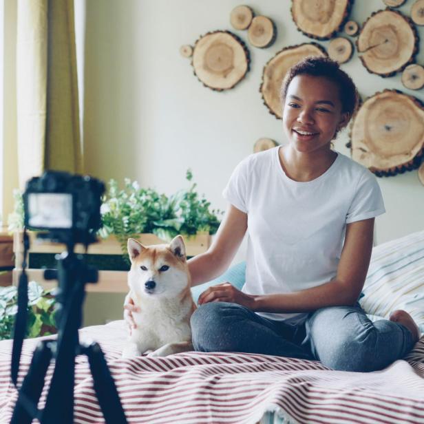 Eine Frau sitzt mit einem Hund auf einem Bett und nimmt ein Video auf.