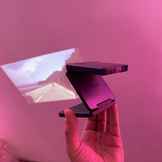 Ein Mini-Beamer der Marke Aurzen ZIP projiziert ein Bild an eine Wand.