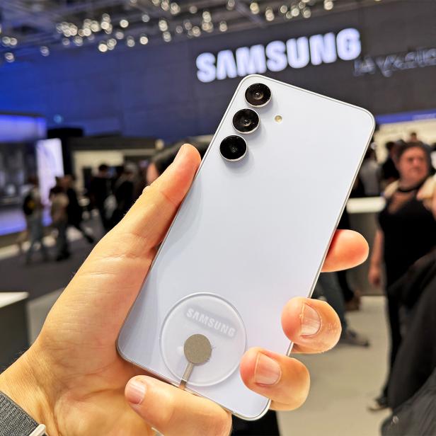 Ein hellblaues Samsung Galaxy S25 FE wird auf einer Messe präsentiert.