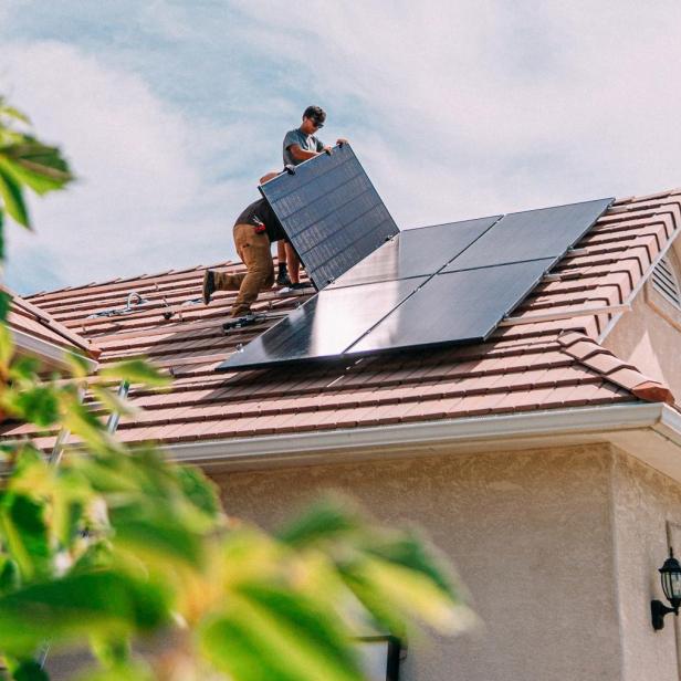 Zwei Arbeiter installieren Solarmodule auf einem Hausdach.