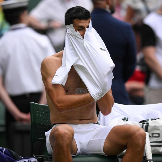 Novak Djokovic zeiht sich ein weißes Shirt an.