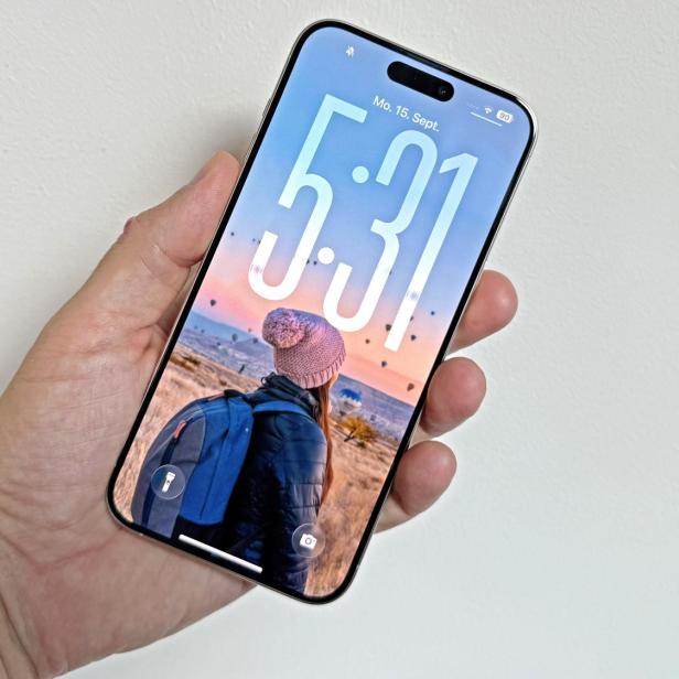 Eine Hand hält ein iPhone mit dem Sperrbildschirm, der eine Frau mit Rucksack in Kappadokien zeigt.
