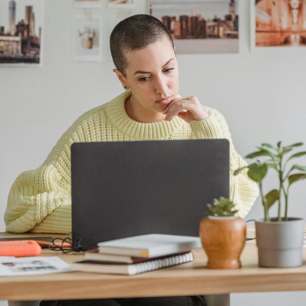 Eine Person sitzt nachdenklich vor einem Laptop an einem Schreibtisch.